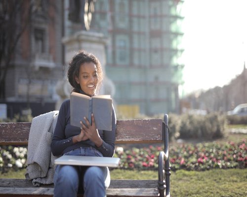 Person relaxing comfortably on a park bench reading a book